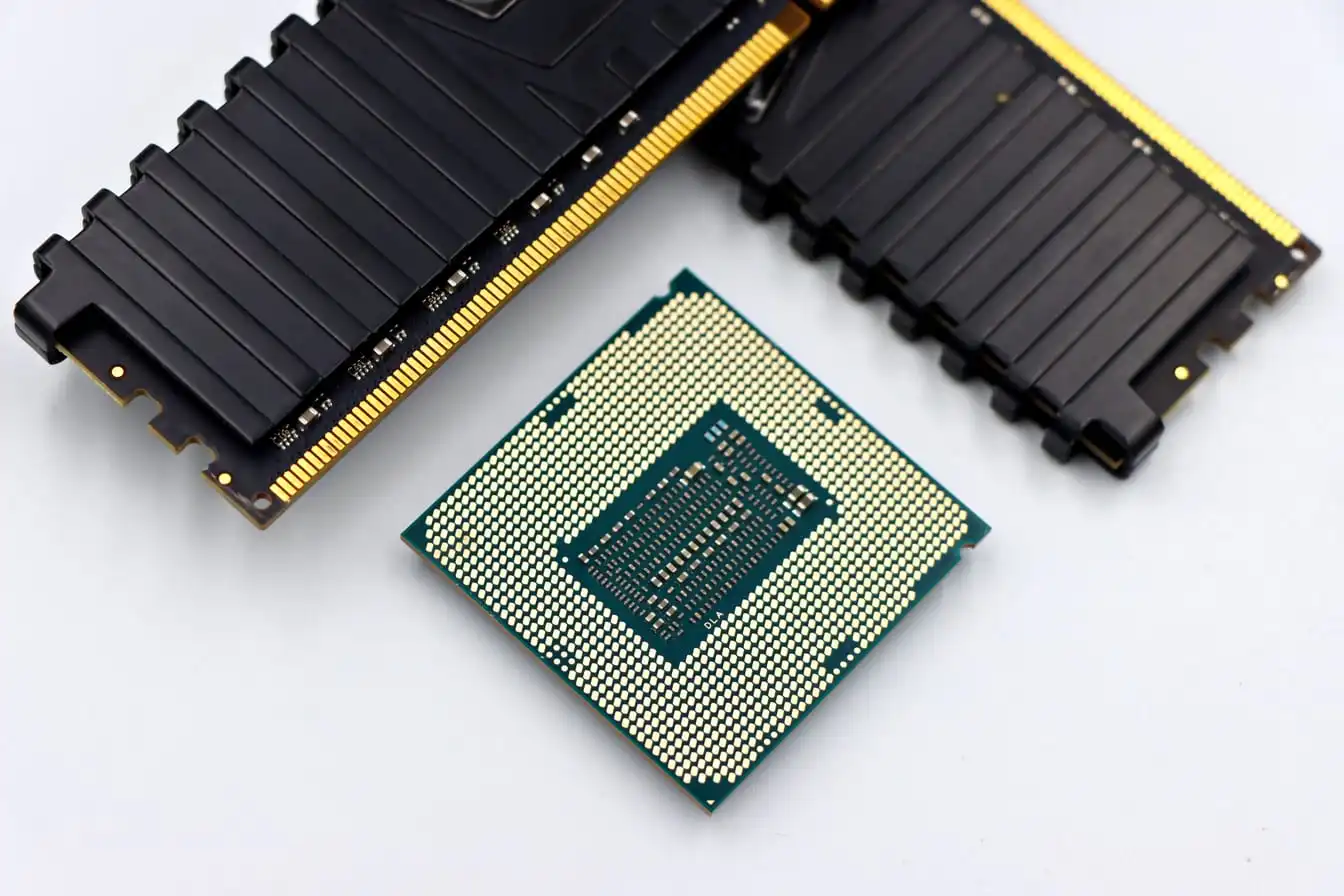 A processor lying pin-side up on a white surface between two black memory modules.