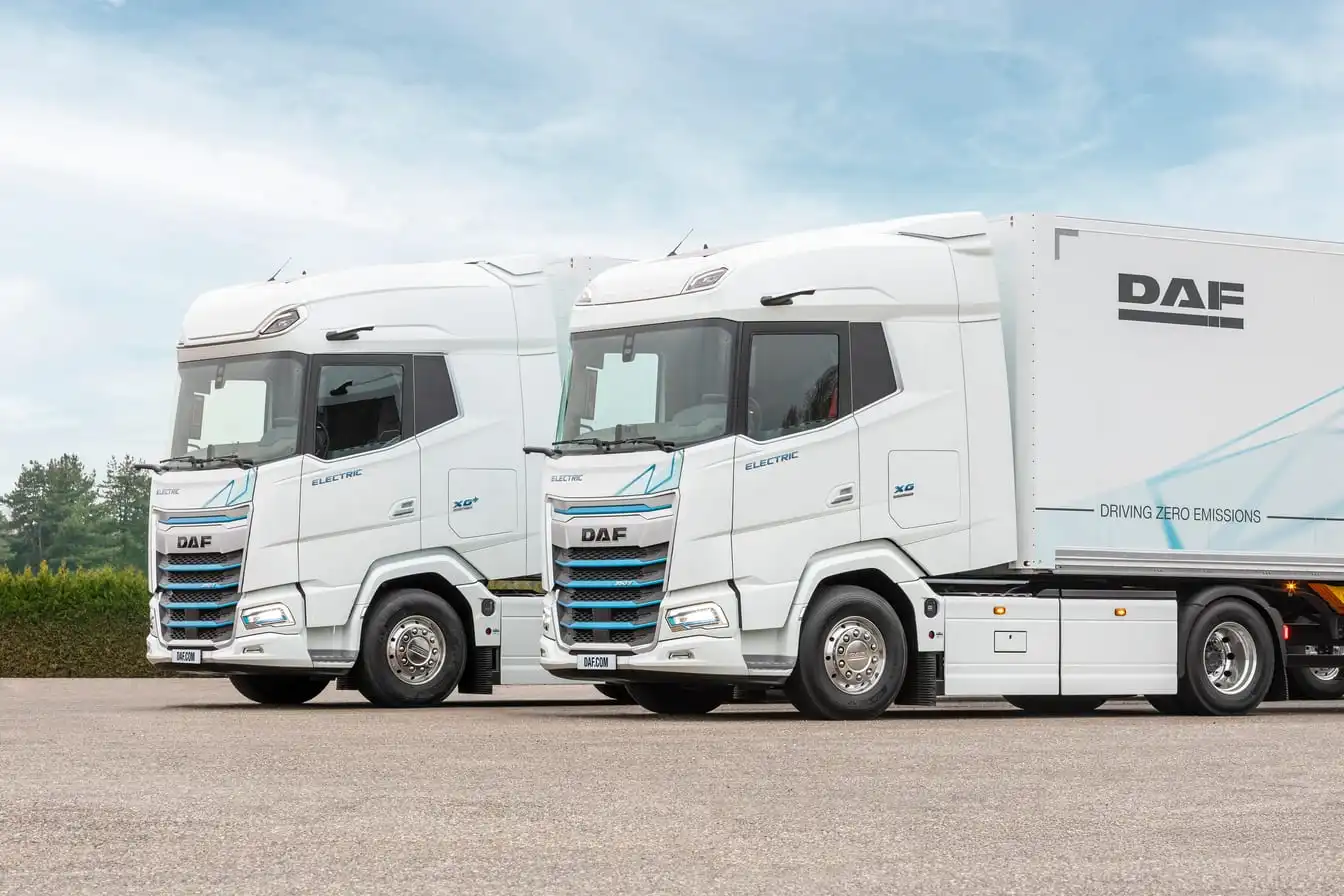 Two white DAF electric tractor units parked side by side on tarmac, the nearer one coupled to a white trailer.