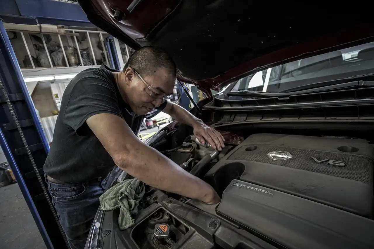 A technician leaning in under the open hood of a car raised on a workshop lift.