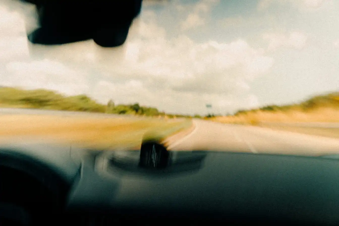 The view forward through a car windshield onto a two-lane road, the verge and trees blurred by the car's motion.