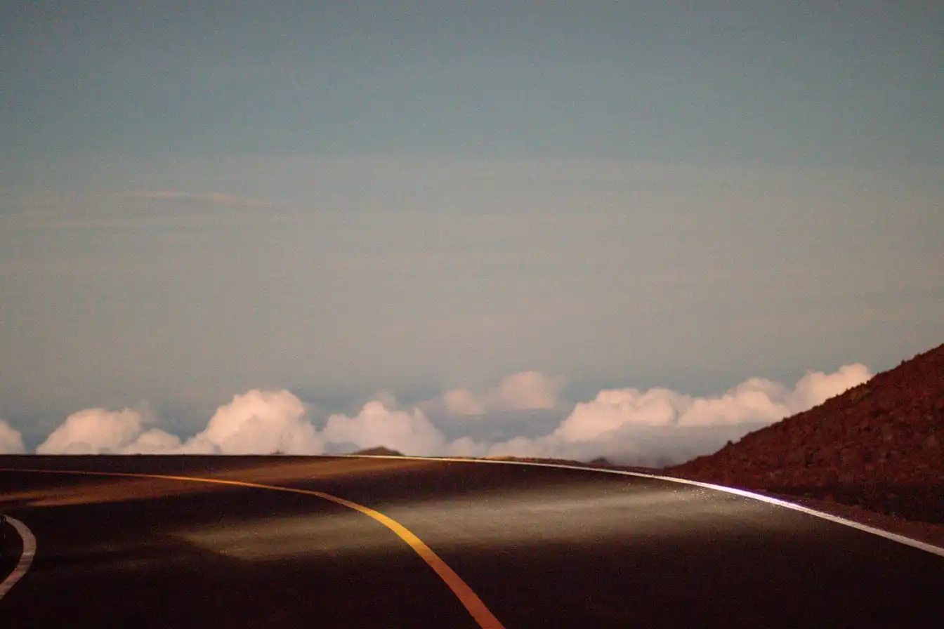 A curved two-lane road climbing into low cloud at dusk.
